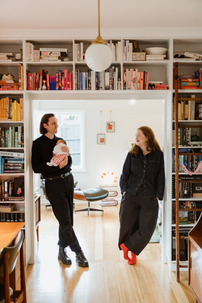 mum and dad stand against a doorframe, surrounded by books on bookcase